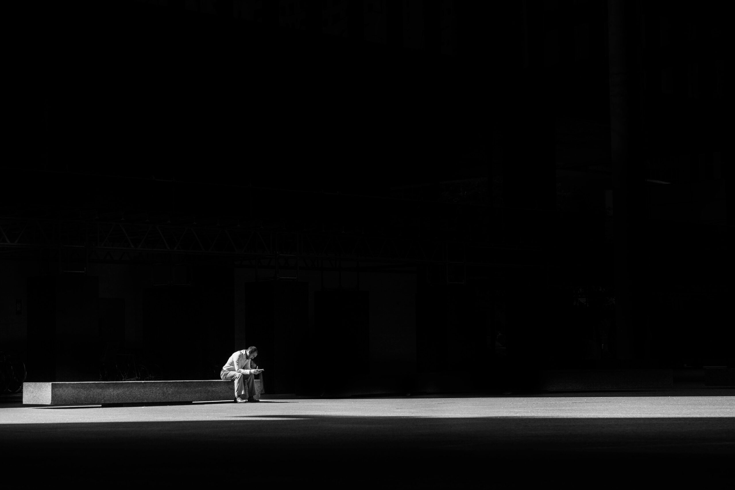 A lone man sitting on a bench, captured in striking black and white, conveying solitude and contemplation.